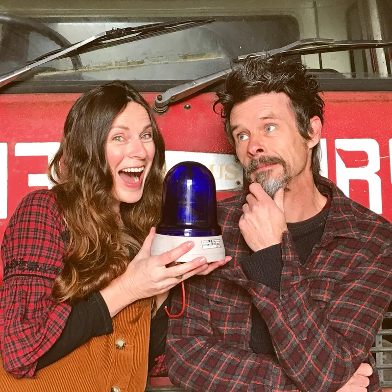 Close up of man and woman with a blue light standing in front of a vintage Bedford fire engine