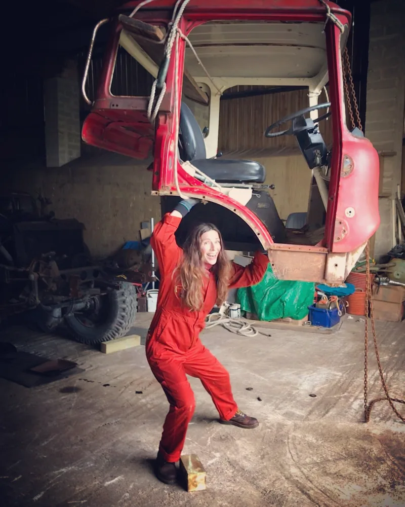 Woman in orange overalls pretending to lift the cab of a Bedford truck