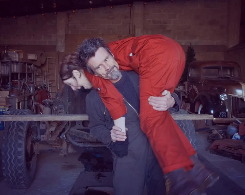 Man lifting a woman in red overalls over his shoulder