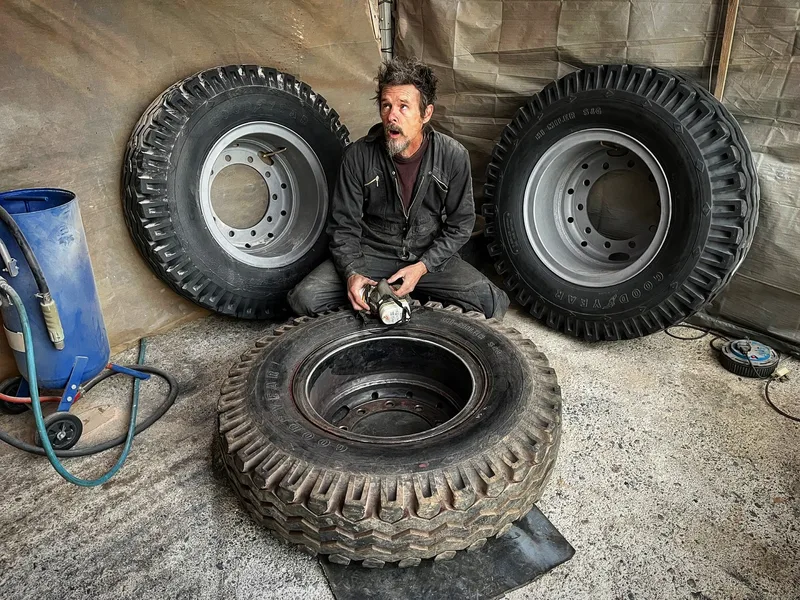 Man in black overalls with a grinding disk and 3 large wheels