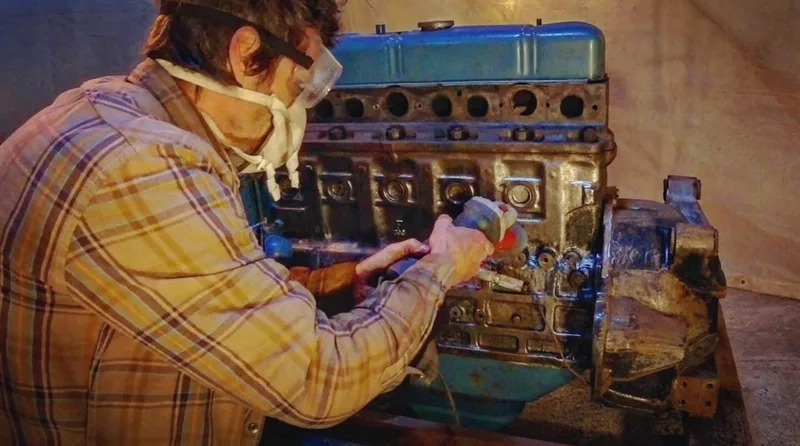 Man grinding the paint off of a truck petrol engine