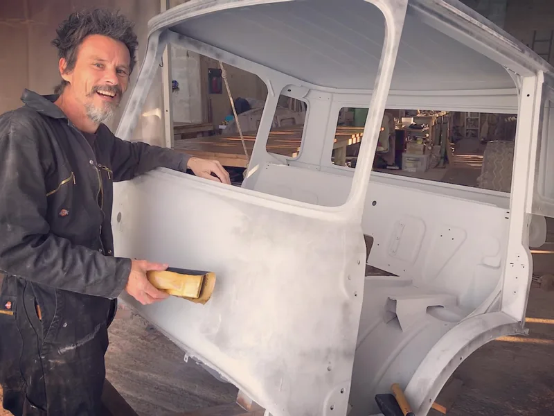 Man in overalls sanding the cab shell of a Bedford truck