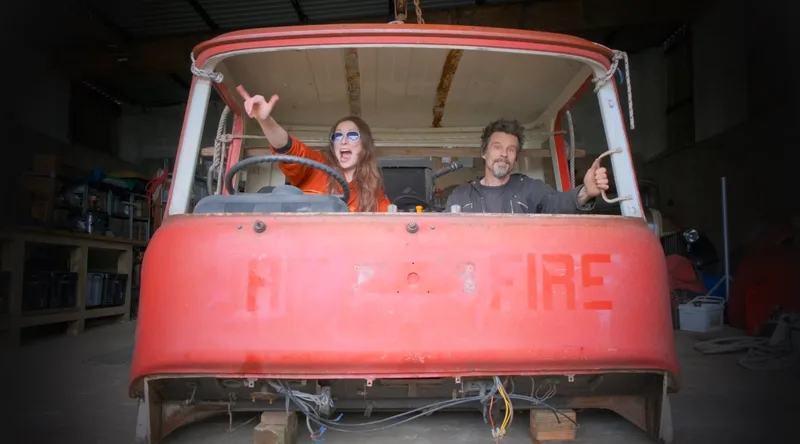 Man and woman inside the disassembled red cab of an old Bedford truck
