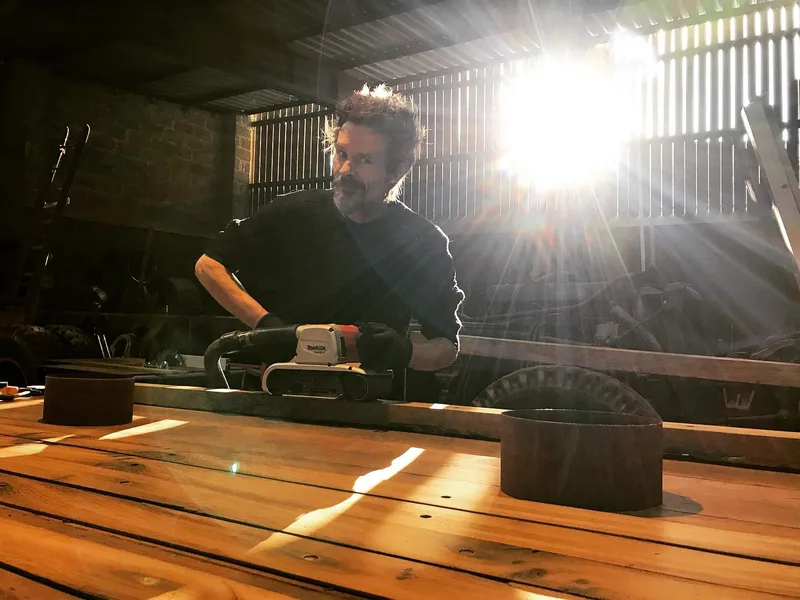 Man sanding wood with sun beams coming through the shutters from behind