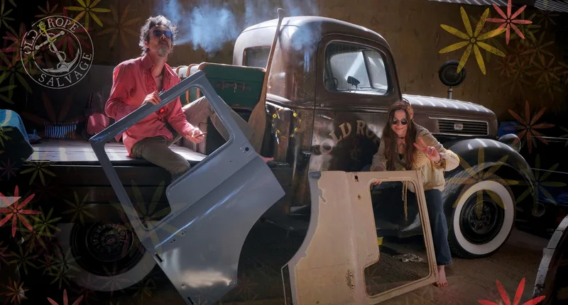 Man and woman sitting on a vintage Ford pick up truck holding the doors of a Bedford truck