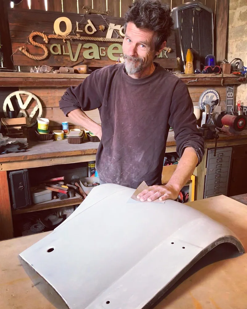 Man standing at workbench sanding a car panel