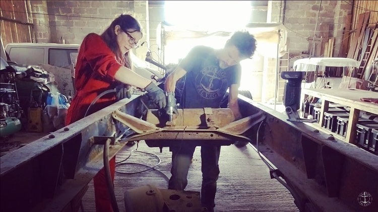 Man and woman in a workshop taking apart the chassis of a vintage Bedford truck