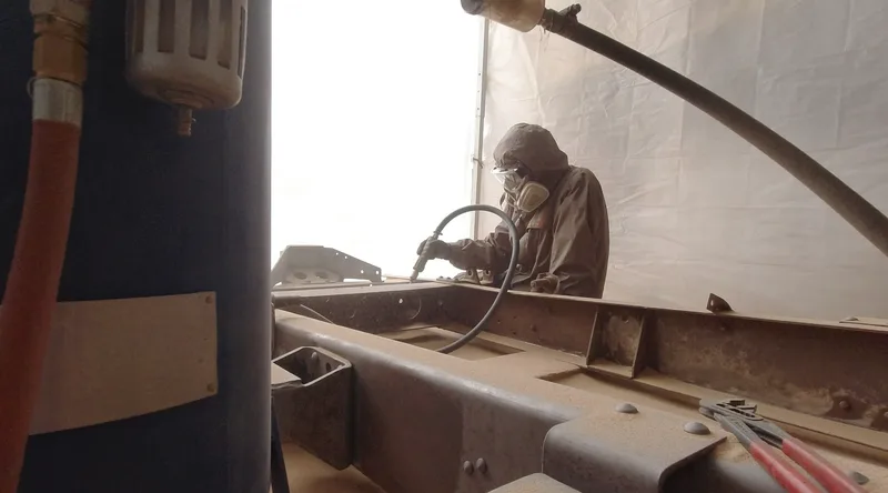 Woman sandblasting a truck chassis frame