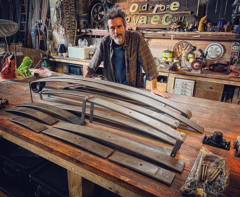 Man standing at a workbench with truck leaf springs in pieces