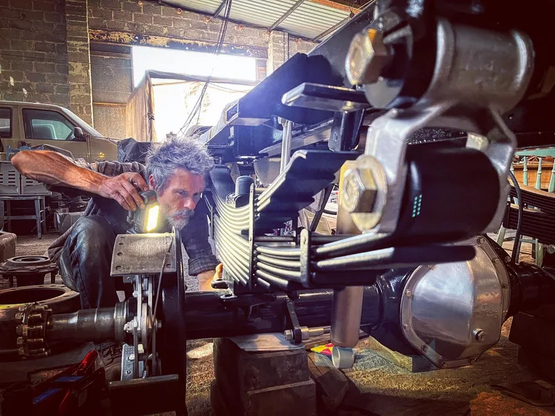 Man with torch inspecting the leaf springs on the back of a 1970s Bedford truck