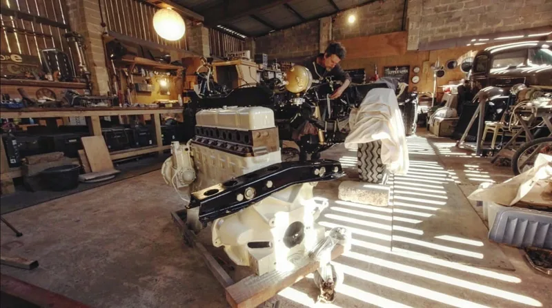 Man working on a vintage Bedford truck in a workshop with a white petrol engine in the foreground