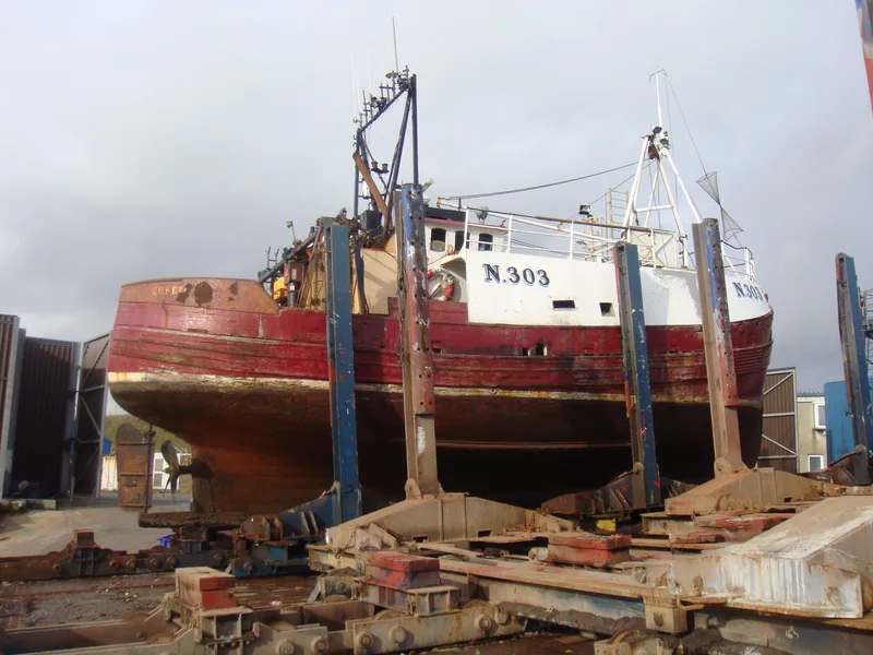 Side view of a Large wooden fishing trawler number N.303 painted red and white out of the water in a dry dock