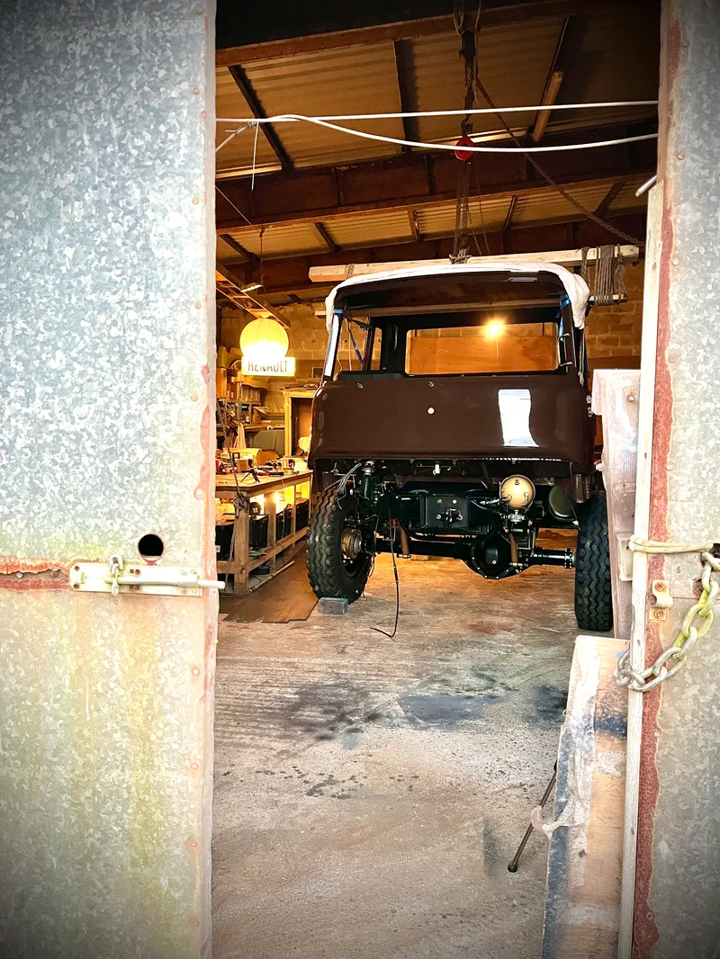 Partly dismantled newly restored brown Bedford truck viewed through the metal doors in to a workshop