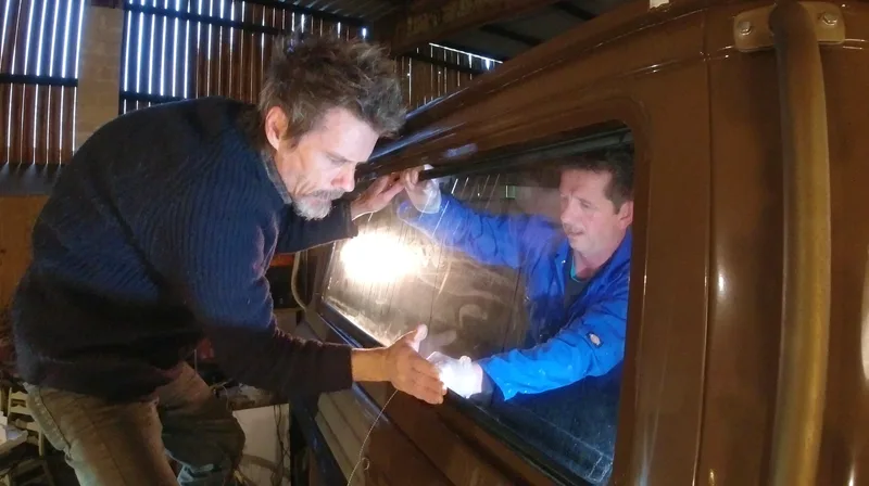 Two men in a workshop fitting the rear window in to a Bedford truck cab
