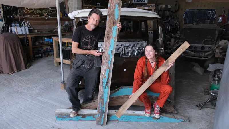 Man and woman in overalls holding old oak beams in front of a Bedford truck cab 