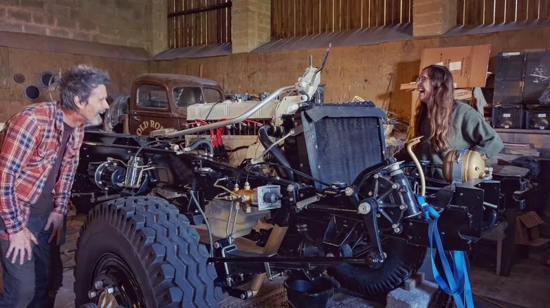 Man and woman laughing on either side of a Bedford truck chassis and petrol engine