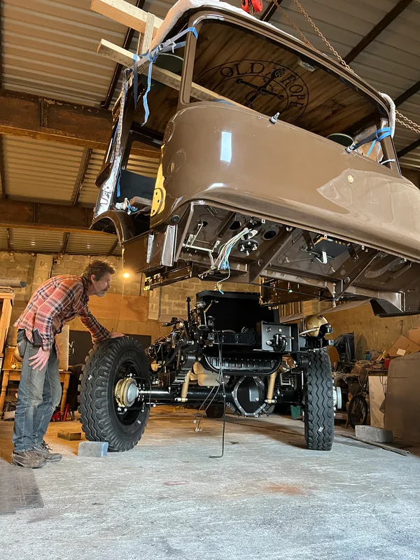 Man with a classic restored Bedford truck with cab getting winched on to the chassis