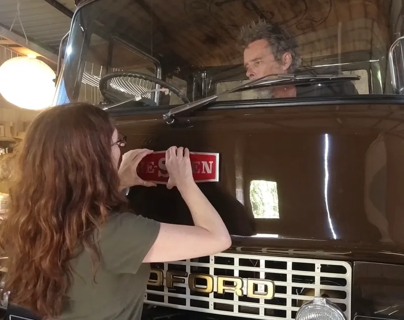 Man and woman fitting the name badge The Siren to a newly restored Bedford truck