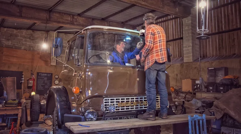 Two men in a workshop fitting the front window in to a 1970s Bedford truck
