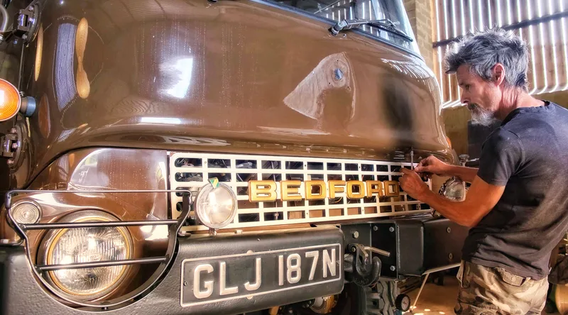 Man fitting a Bedford name badge to a newly restored Bedford truck painted in brown