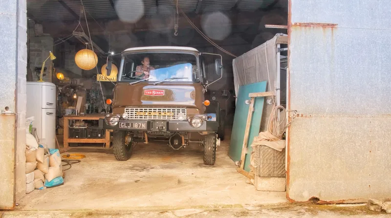 Man driving a brown restored Bedford truck out of a workshop